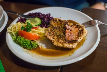 Grilled pork steak with fresh vegetable on white plate in restaurant.