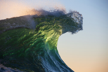 Beautifully textured back-lit emerald ocean wave curling under a warm sunrise