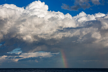 Beautiful vibrant rainbow descending from the clouds to a dark blue sea