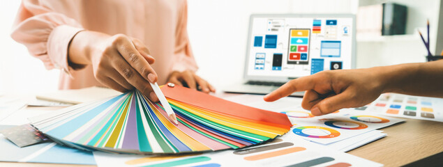 Cropped image of interior designer chooses color from color swatches while laptop displayed UI and...