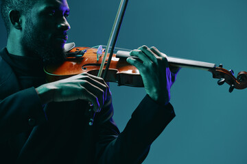 Classical musician in elegant attire performing on violin under a soft blue spotlight on stage with...
