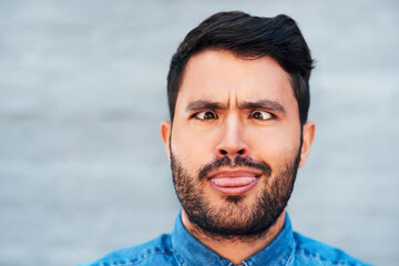 Comic, crossed eyes and man with tongue out, silly and portrait outside by brick wall. Male...