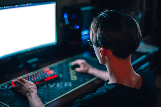 A young man works at a computer in a dark room. Monitor with blank screen. A teenager sits at a computer at night.