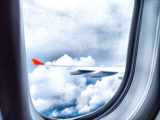 Clouds and a wing through a porthole in an airplane. Aerial View of Fluffy Clouds and Airplane Wing...