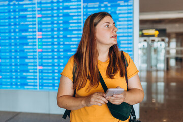Happy Caucasian 30s Woman with phone search for international registration. 30s female checking Trip Destination on Internet near information board. Tourist journey trip concept