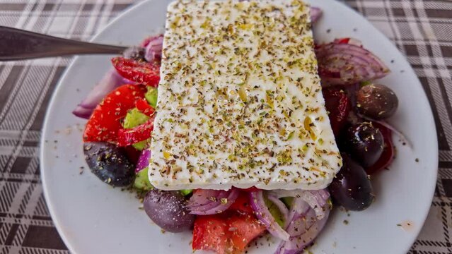 Close-up of Greek salad with feta cheese topped with herbs on a plaid tablecloth