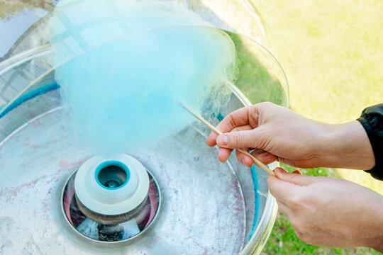 Close up view of person hands spinning blue color cotton candy with machine. Spin around wood stick. 