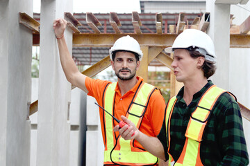 Two happy smiling worker engineers with safety vest and helmet inspecting working area at construction site. Architect working together at ground level of building site workplace. Labor construction