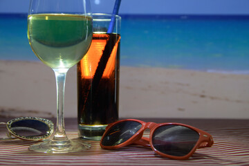 A glass of wine and a glass of soda sit on a table next to a pair of sunglasses. Night cocktail on...
