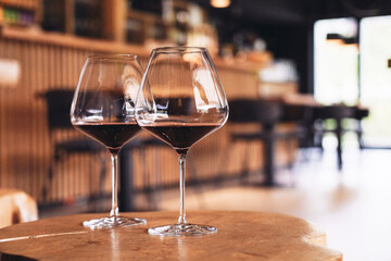 Two glasses of red wine on a wooden table, restaurant and bar on the background 