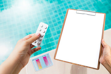 Water testing tablets in girl hand with blank report sheet on clipboard over swimming pool background ,water tester test kit on swimming pool edge, summer outdoor day light, water quality check