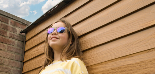 A girl wearing sunglasses and a yellow shirt is smiling at the camera