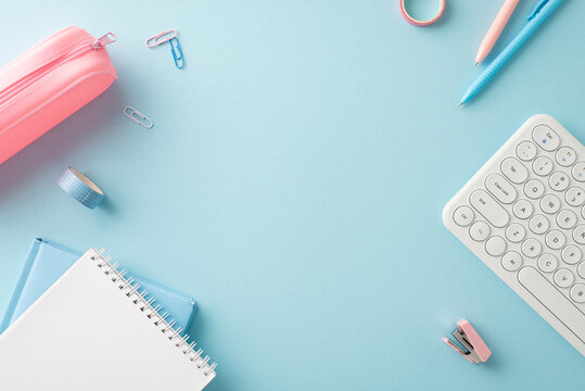 A neatly organized desk setup featuring school and office essentials such as notebooks, pens, and a keyboard, perfectly arranged on a light blue background