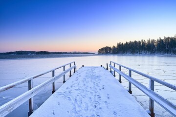 Wooden dock blanketed with snow, extends out onto a pristine, frozen lake.