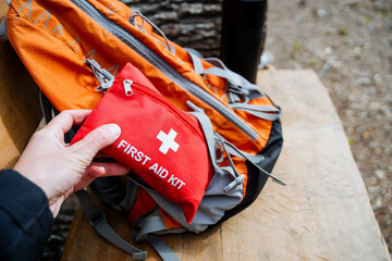 A person holding a first aid kit in front of a backpack