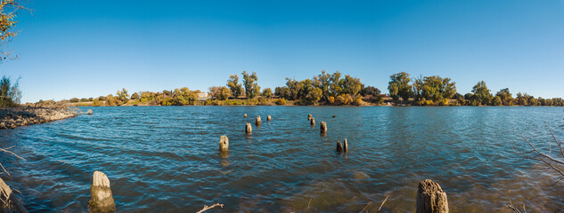 Serene lake shore, featuring wooden poles in the foreground protruding out of the water.