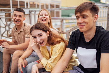 Four teenagers in casual clothes chat and laugh on the roof of the house. Girls and boys have fun together. Funny students relax and walk.