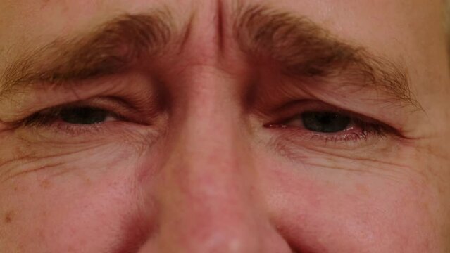 Close-up gray eyes of unhappy crying man. A male person looking at camera feeling depression and upset.