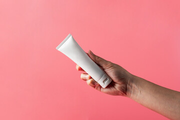 Plastic white tube for cream or lotion. Skin care or sunscreen cosmetic with hand on pink...