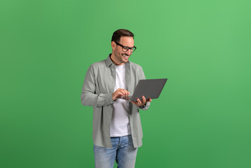 Portrait of happy handsome entrepreneur checking e-mails online over laptop against green background