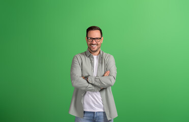 Young handsome freelancer in glasses smiling at camera and standing confidently on green background
