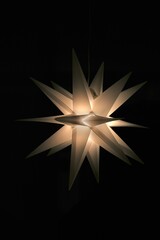 Single illuminated monochrome Christmas star hanging against a black background
