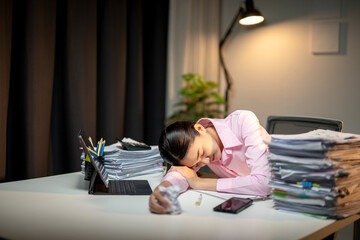 A woman in a pink shirt is sleeping on a desk with a laptop and a cell phone
