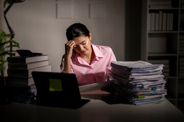 A woman is sitting at a desk with a stack of papers in front of her