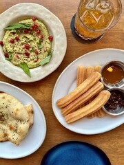 Baked naan is served with green hummus, and churros are served with caramel and chocolate dips