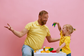 Charming young boy and his father enjoy playful building time with colorful blocks against pink...