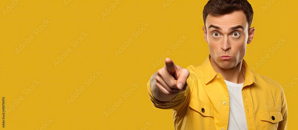 Poster A young man with an expression of embarrassment on his face is pointing towards something on a yellow background in a copy space image