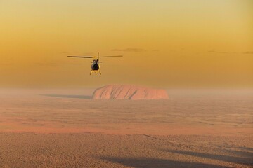 Helicopter flying over an expansive desert with Uluru in the background. Australia