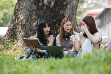 Happy Asian teenage female college students tutor together in the garden outside the university classroom. Female students happily help each other with their homework.