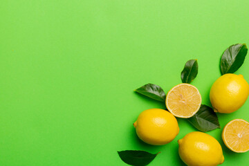 Many fresh ripe lemons with green leaves on colored background, top view, space for text