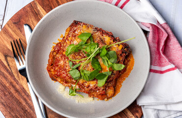 A bowl of traditional lasagne served in a white round bowl, on top of a circular wooded chopping board