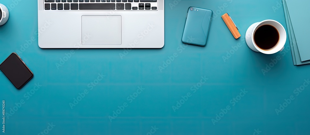 Poster A top down view of a blue office desk adorned with a laptop smartphone and various work essentials A cup of coffee sits nearby and there is empty space for adding text This is a designer s workspace