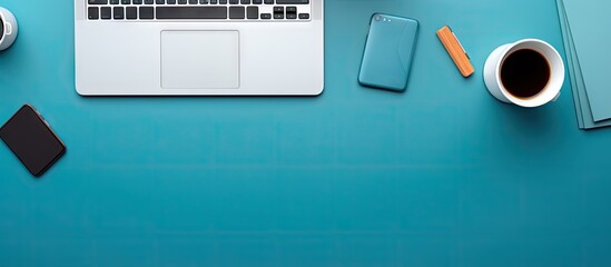A top down view of a blue office desk adorned with a laptop smartphone and various work essentials A cup of coffee sits nearby and there is empty space for adding text This is a designer s workspace