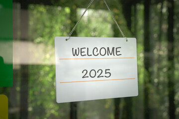 Welcome 2025 on a signboard, hanging on a glass door.