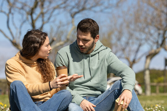 couple in park arguing because they disagree. Young couple on a sunny day arguing about housework or work. Couple talking seriously outdoors in a park.
