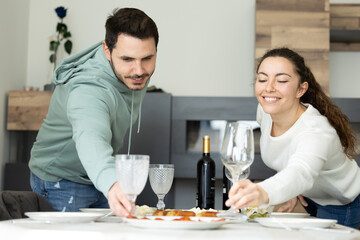 couple setting the table for lunch or dinner with guests. Cheerful caucasian couple setting cutlery for easter dinner.