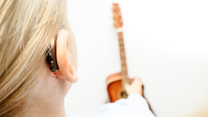 A woman with a hearing aid plays the guitar. I can hear music again! Technologies to assist people with disabilities.