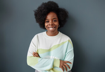Minimal waist up portrait of smiling Black woman with natural hair standing against grey wall...