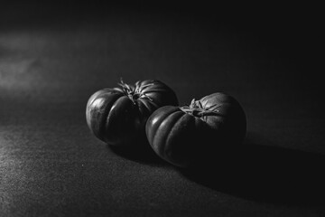 Grayscale shot of two ripe Spanish tomatoes on a solid tabletop, isolated on a blank background