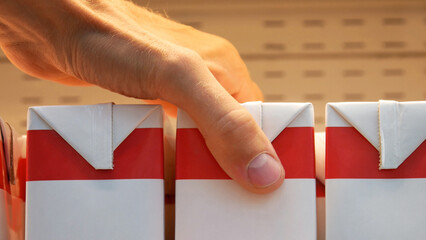 Close-up of a male buyers hand taking a carton of milk from a supermarket fridge shelf