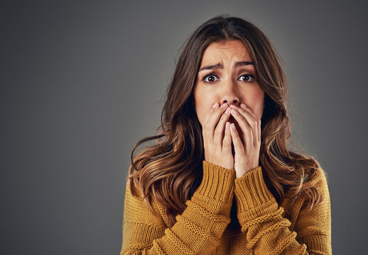 Portrait, scared and woman with fear, afraid and anxiety with secret news on grey studio background. Face, person and model with surprise, shocked and cover mouth with emotions and emoji of gossip
