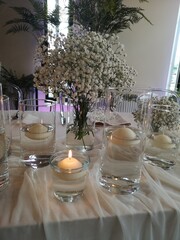 the table has several glass vases holding candles and greenery