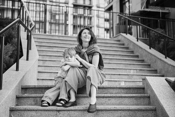Happy family: mother and child son hugging and laugh sitting on the city stairs. motherhood...