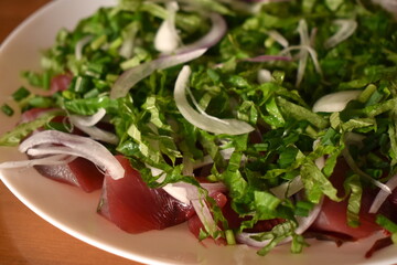 Fresh bonito sashimi topped with shiso, thinly sliced onions, green onions, and seasonings 