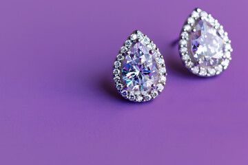 A detailed shot of a pair of elegant diamond earrings on a solid purple background
