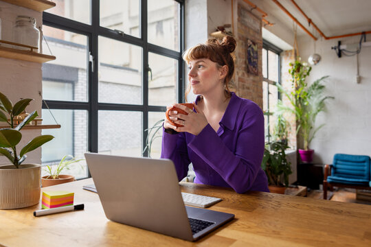 Young adult female student working from a cafe looking out of the window thinking